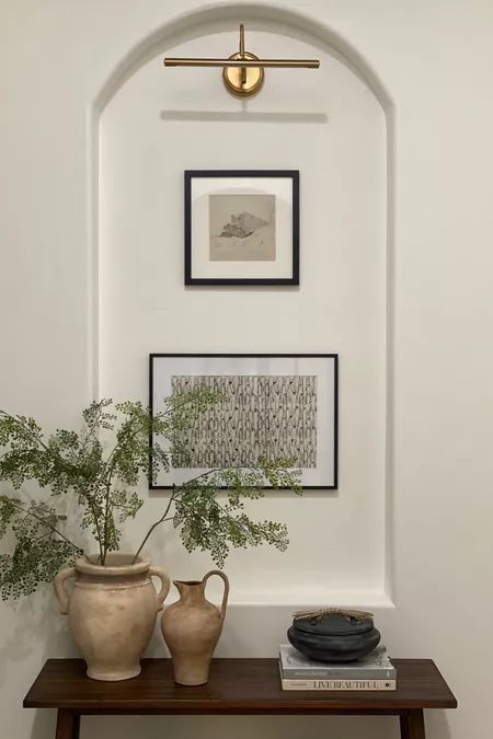 two vases are sitting on a table in front of a wall with framed pictures