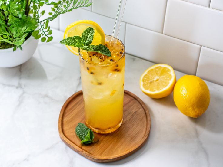 a drink with lemons and mint on a wooden tray next to a potted plant