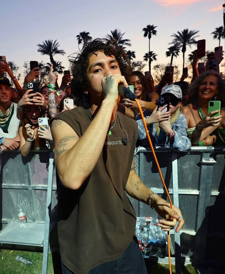 a man standing in front of a crowd holding a cell phone to his ear and singing into a microphone