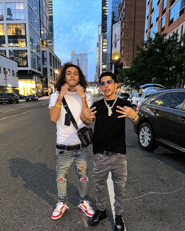 two young men standing next to each other on a street with tall buildings in the background