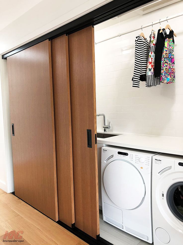 a washer and dryer sitting in front of a wooden door with clothes hanging on it