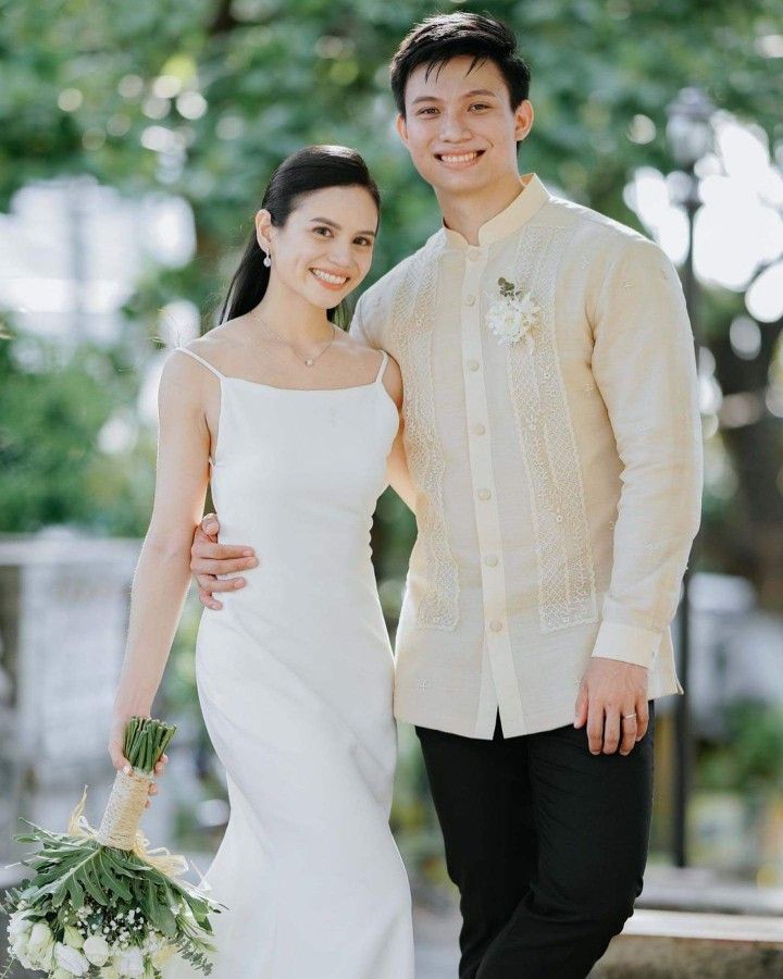 a man and woman standing next to each other in front of some trees with flowers