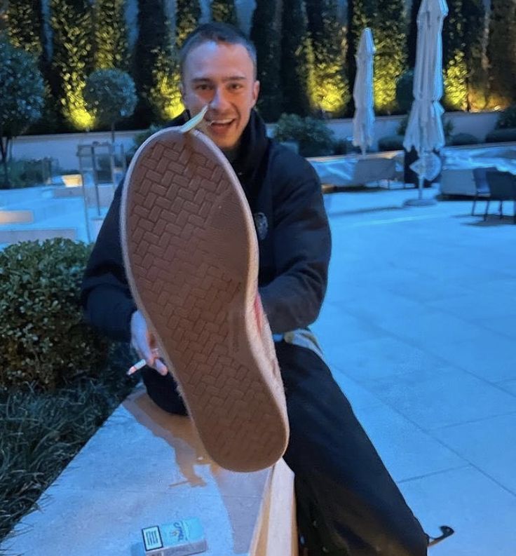 a man is sitting on a ledge with his foot in the air and smiling at the camera