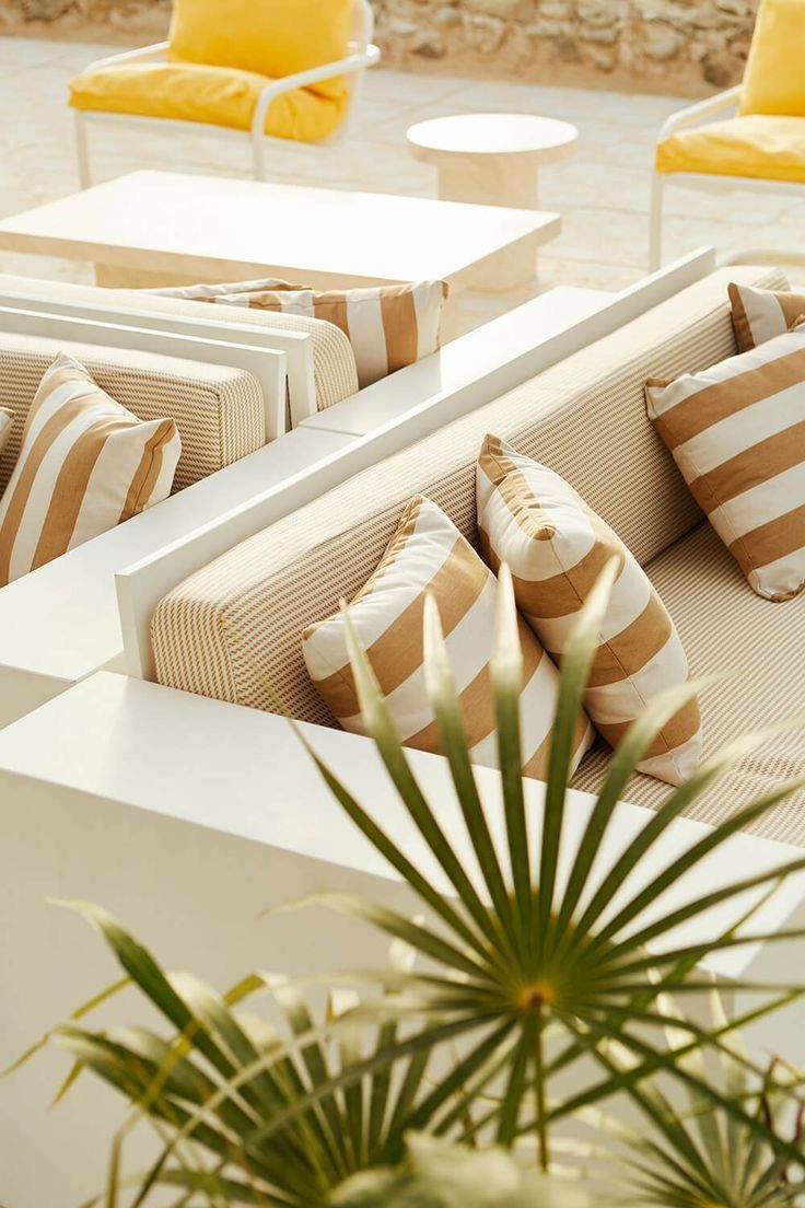 an outdoor seating area with yellow and white striped pillows on the couches next to a potted plant