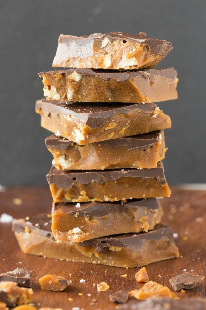 a stack of pieces of chocolate on top of a wooden cutting board next to nuts