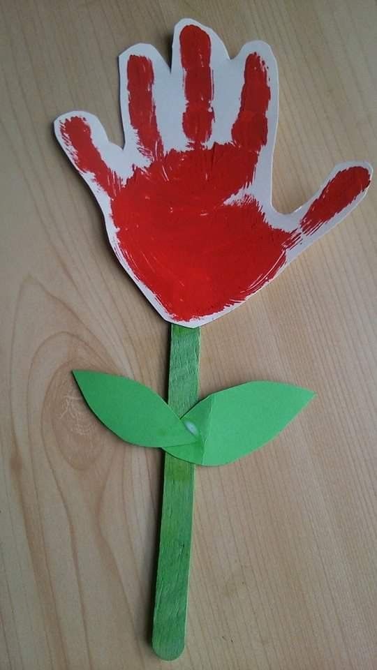 a handprinted red flower on a wooden stick with green leaves in front of it