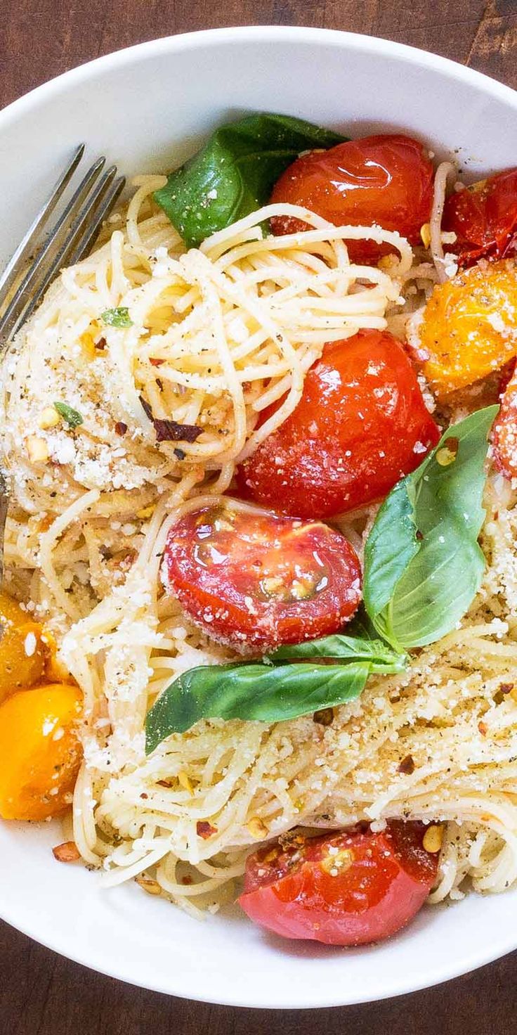 a white bowl filled with pasta, tomatoes and spinach on top of a wooden table