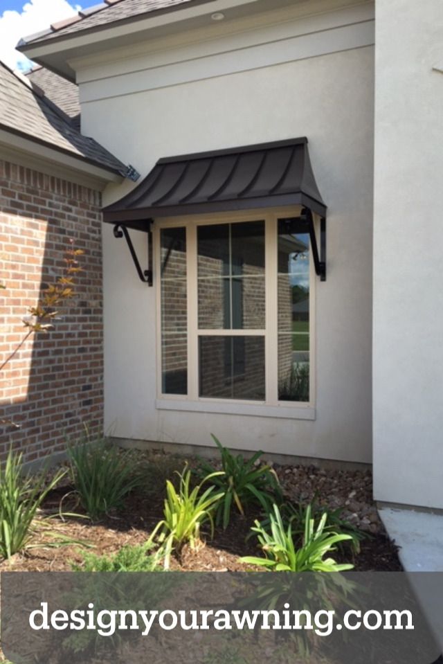 a white house with a black awning on the front door and windows above it