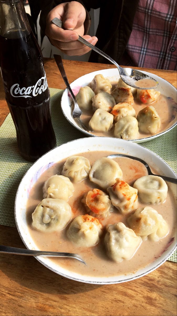 two white bowls filled with dumplings on top of a table next to a coke