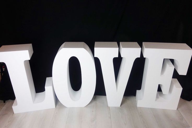 the word love is made up of white letters on a wooden floor in front of a black background