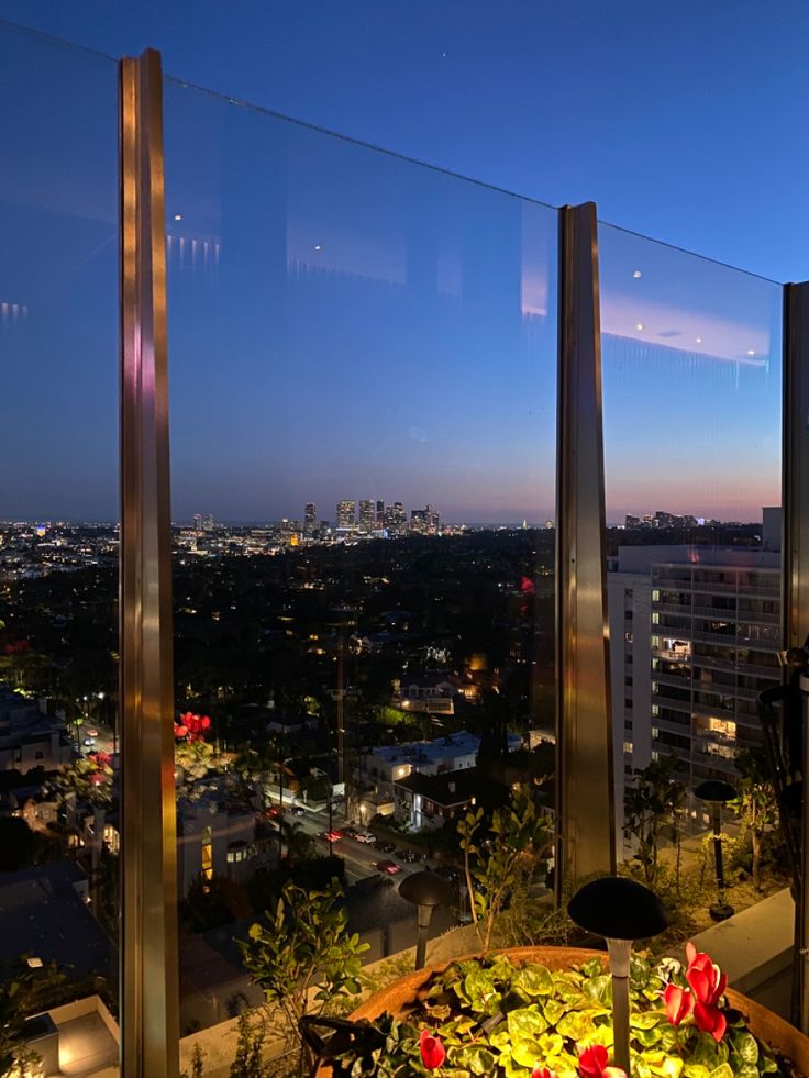 a table with flowers on it in front of a window overlooking the city at night