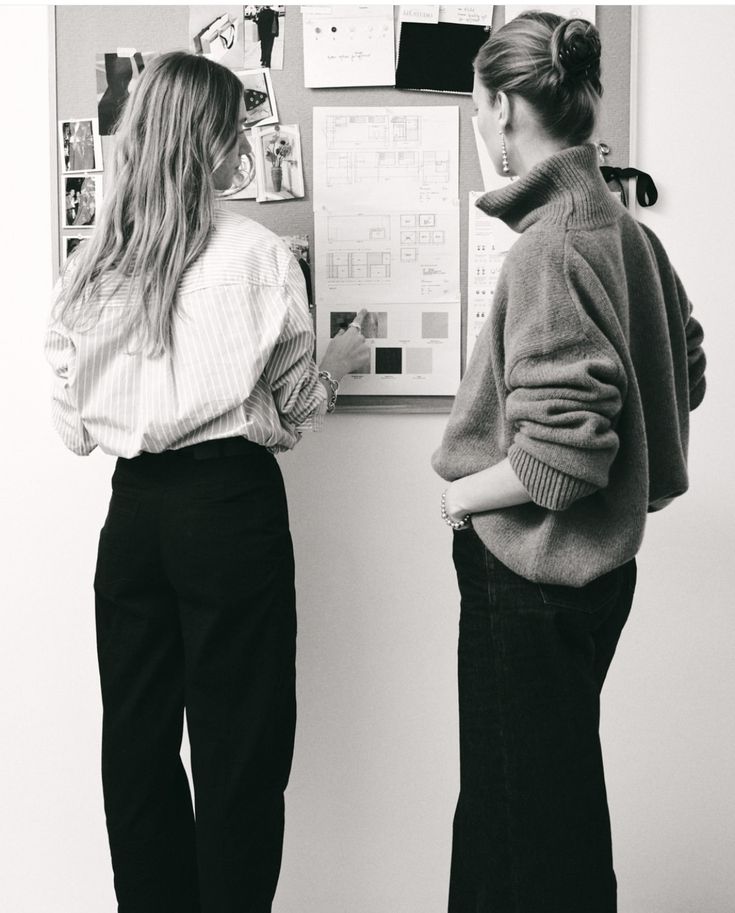 two women standing next to each other in front of a wall with pictures on it