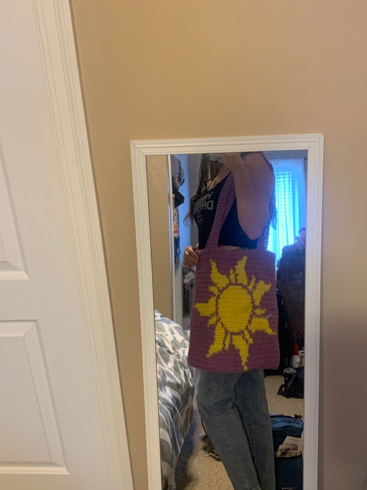 a woman standing in front of a mirror holding a crocheted sunflower bag