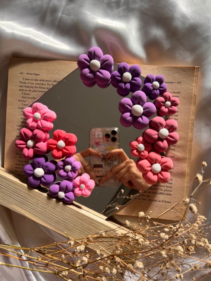 an open book with flowers on it and a person taking a photo in the mirror