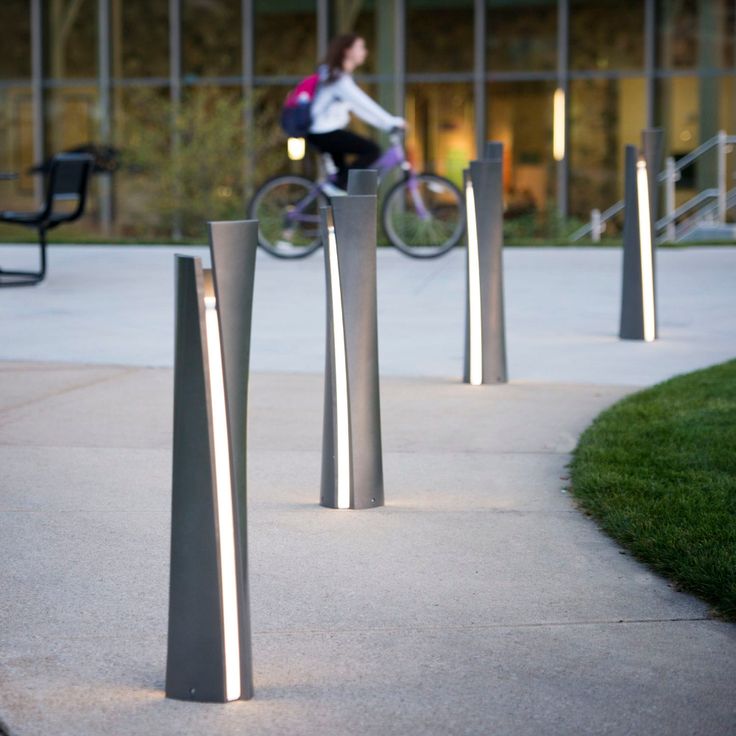 a person riding a bike on a sidewalk near some benches and chairs with lights in the background