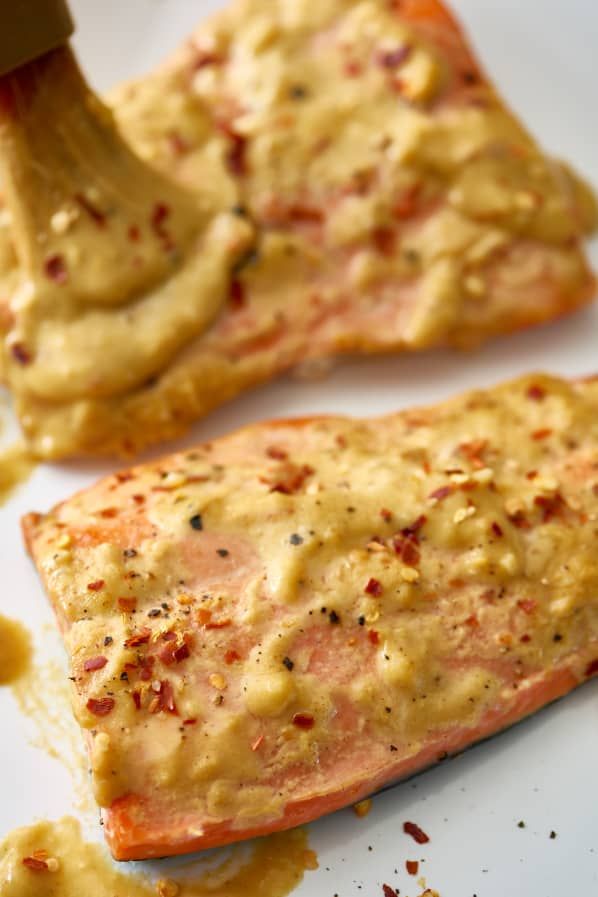 two salmon fillets on a white plate with mustard and seasoning being drizzled over them