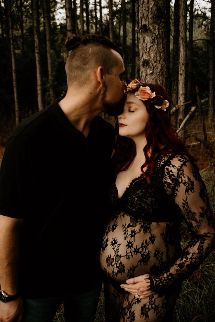 a pregnant couple kissing in the woods