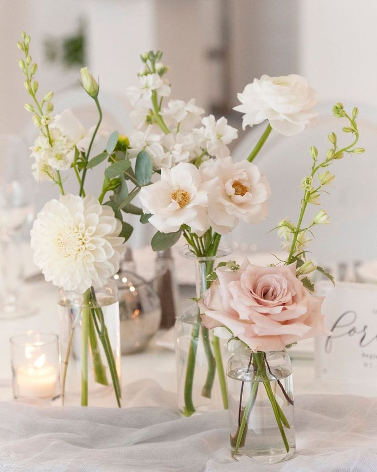 two vases filled with flowers sitting on top of a white tablecloth covered table