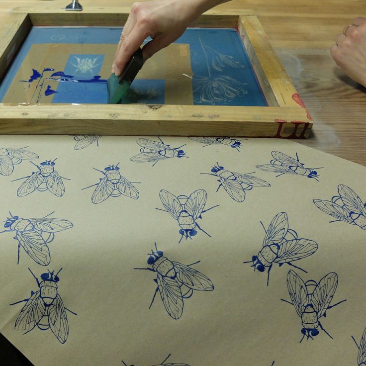 a person using a stencil to draw bees on a sheet of paper with blue ink