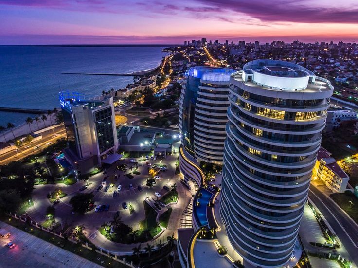 an aerial view of the ocean and city skyline at night, with buildings lit up