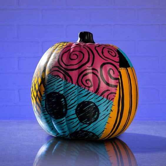 a colorful painted pumpkin sitting on top of a reflective surface next to a brick wall