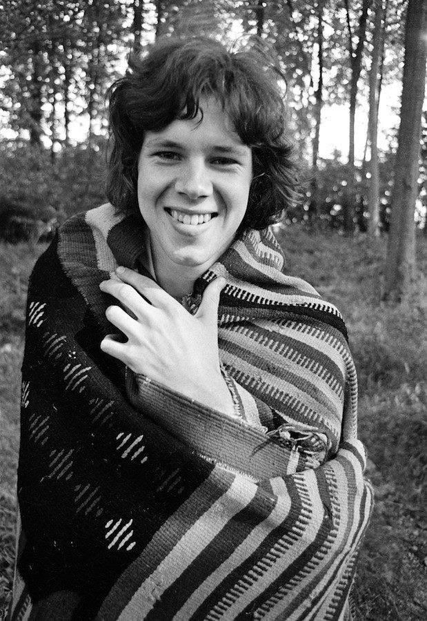 black and white photograph of woman wrapped in blanket smiling at camera with trees in the background