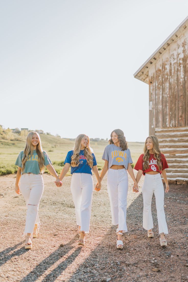 three girls are walking down the dirt road holding hands and one girl is wearing a blue shirt