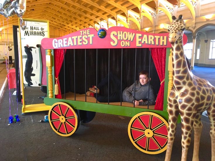 a fake giraffe is standing next to a man in a toy train that says the greatest show on earth