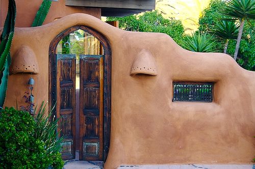 an adobe - style house with arched doorways and cactus trees in front of it