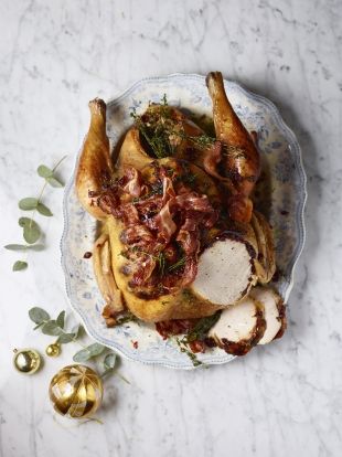 a roasted chicken with onions and herbs on a platter next to christmas baubles