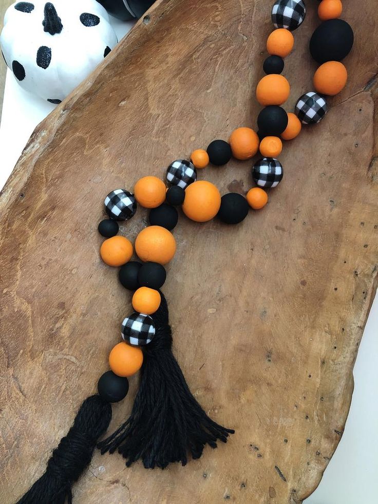 an orange and black beaded necklace with tassels on a piece of wood