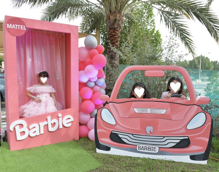 two women in pink dresses are sitting in a barbie car with balloons attached to it