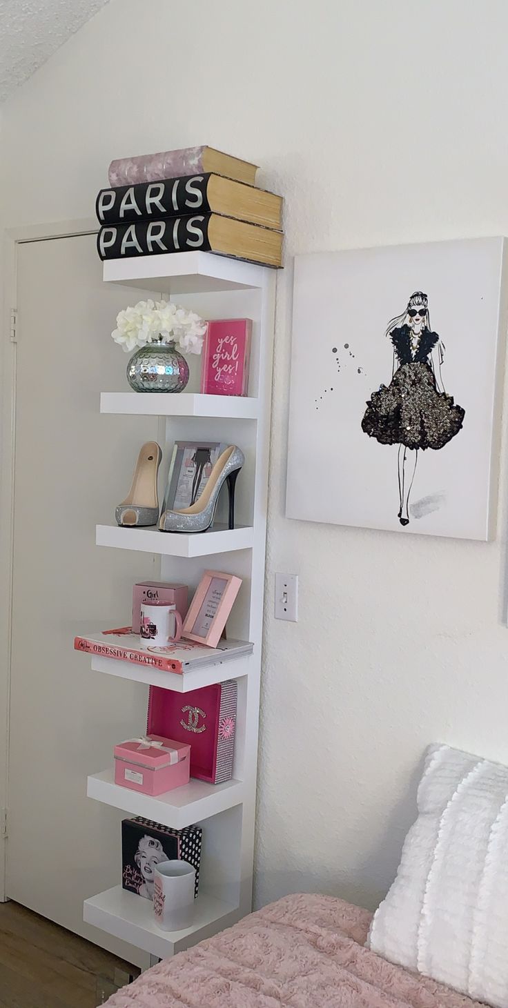 a white book shelf filled with lots of books next to a pink and white bed