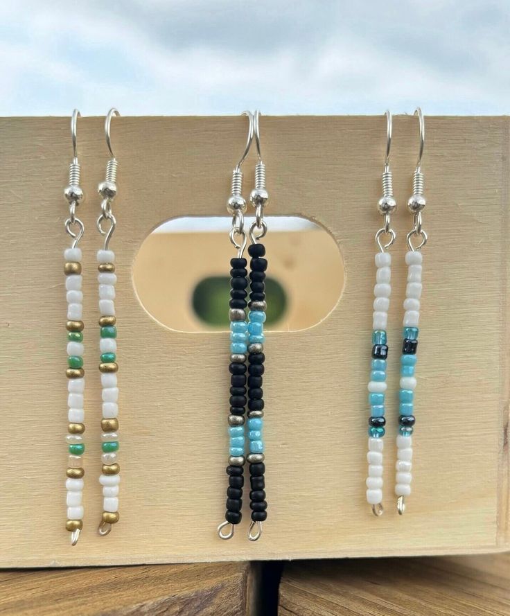 four beaded necklaces are hanging on a piece of wood