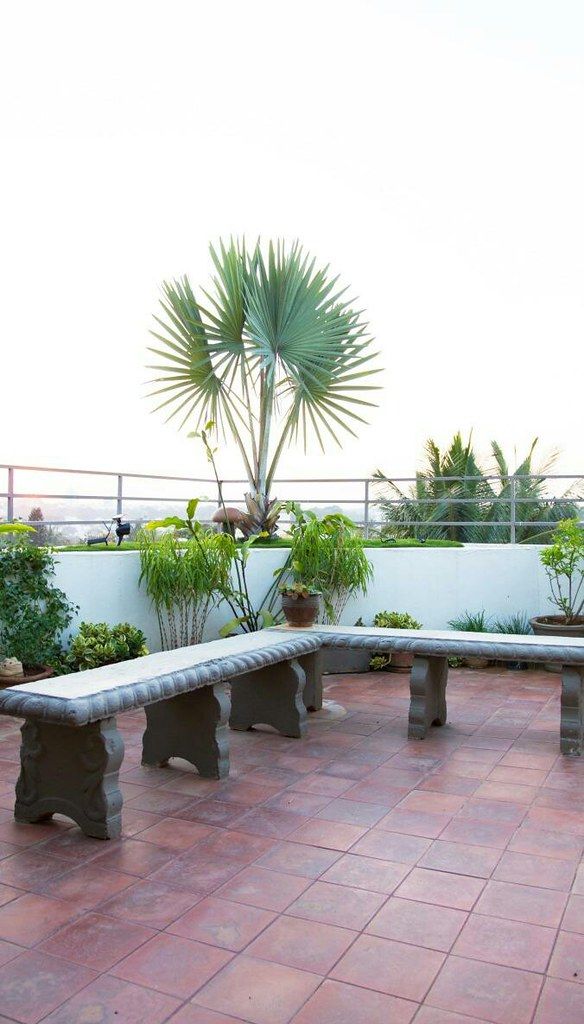 a bench sitting on top of a brick floor next to a planter filled with potted plants