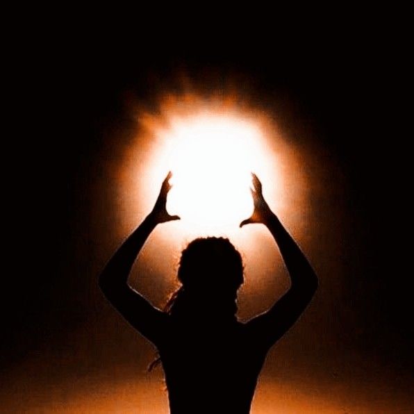 the silhouette of a woman holding her hands up in the air with light shining behind her