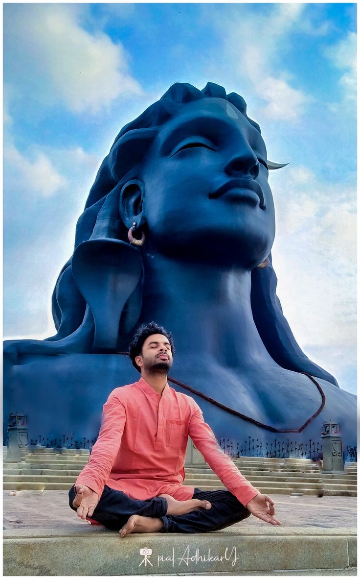 a man sitting on the ground in front of a large blue statue with his eyes closed