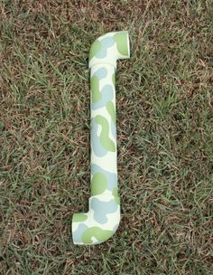 the letter j is made out of camouflage fabric and sits in the middle of some grass