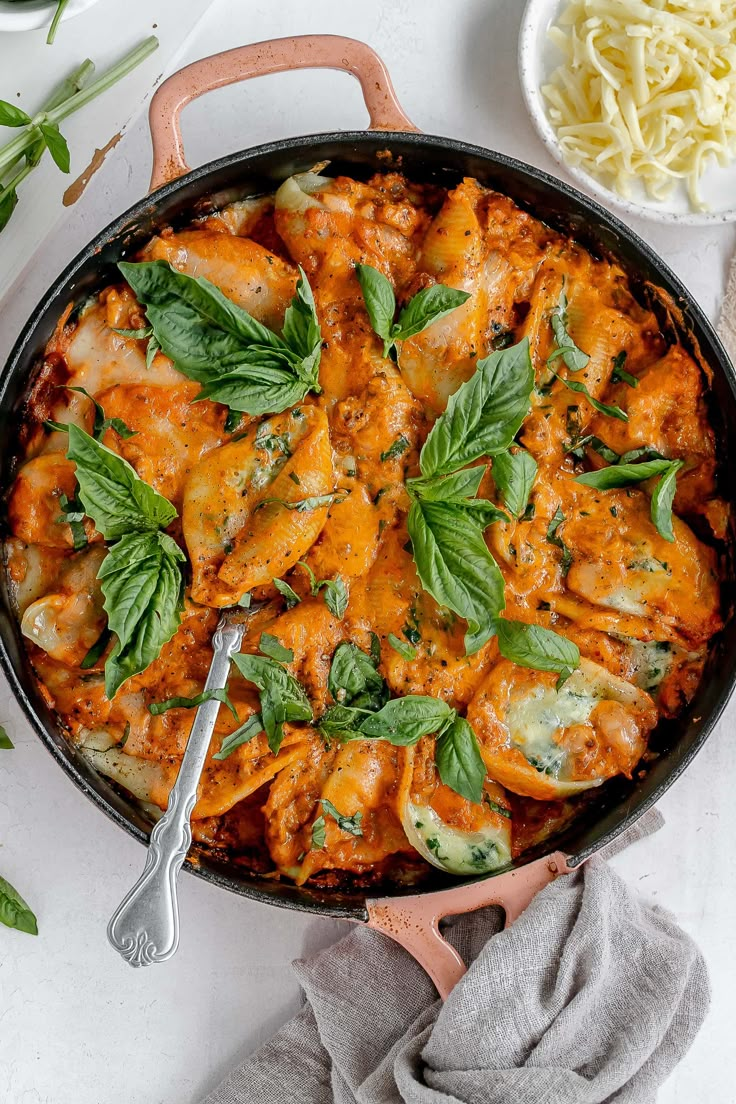 a skillet filled with chicken and spinach covered in sauce, garnished with fresh basil