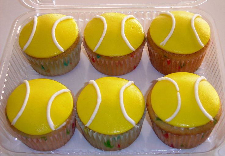 cupcakes with yellow frosting and tennis balls on them in a plastic container