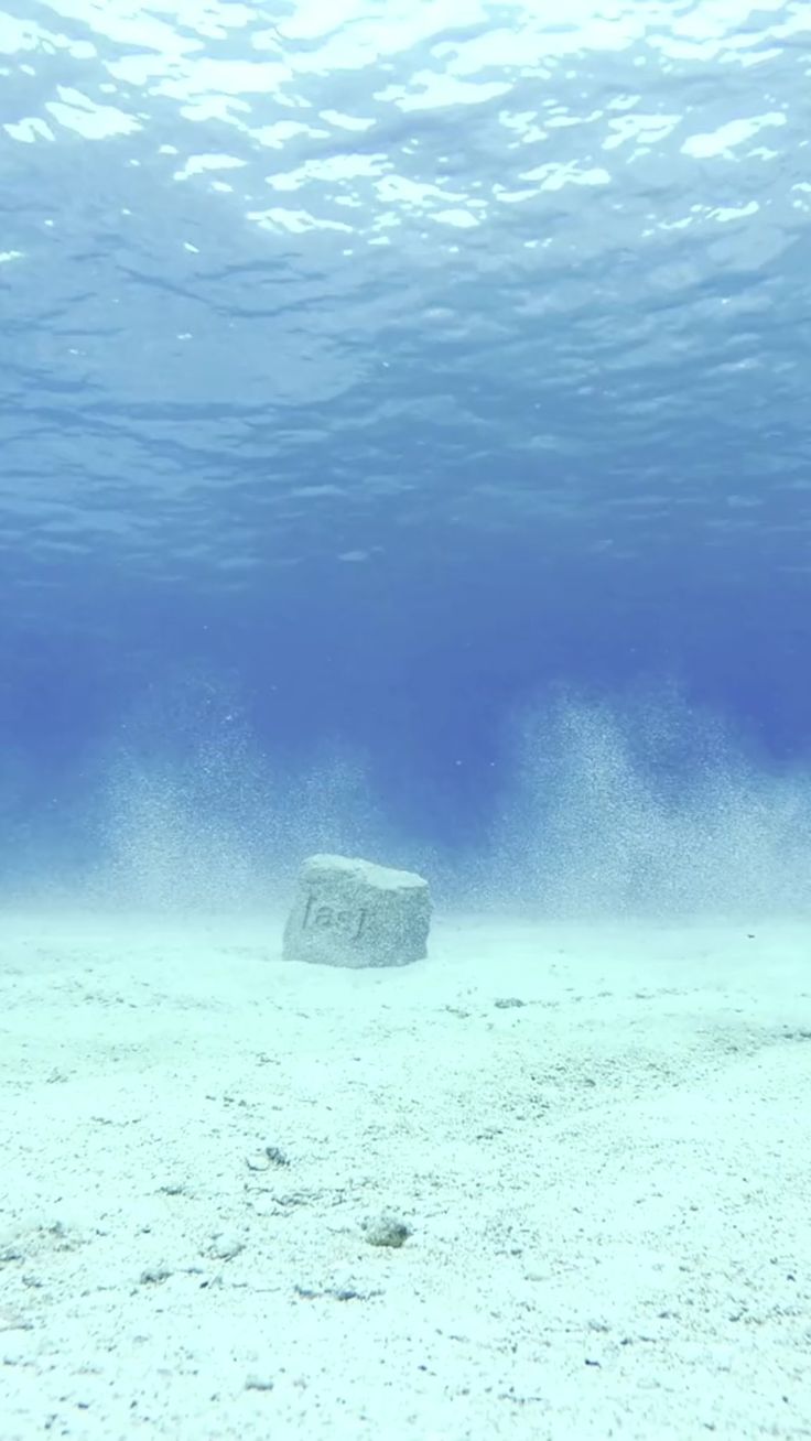 an underwater view of the ocean with rocks and sand in the foreground, under water