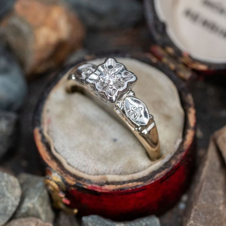 an engagement ring sitting on top of a wooden box next to some rocks and stones