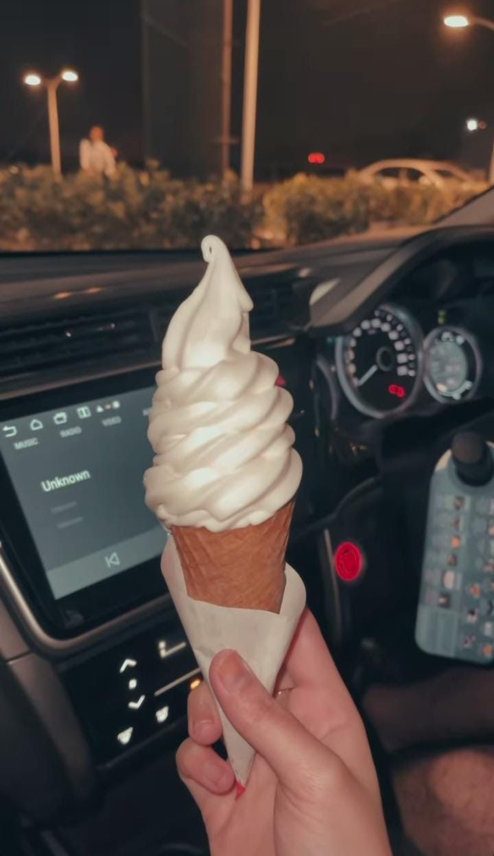 a person is holding an ice cream cone in their hand while driving the car at night