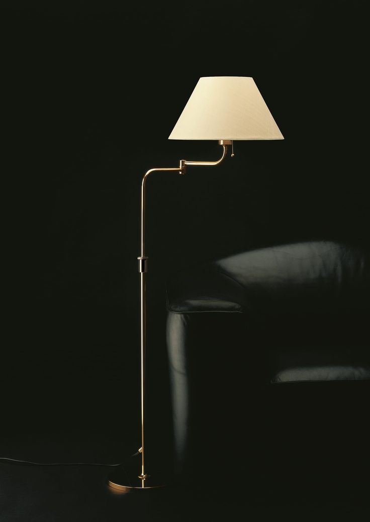 a floor lamp with a white shade on it in a dark room next to a black chair