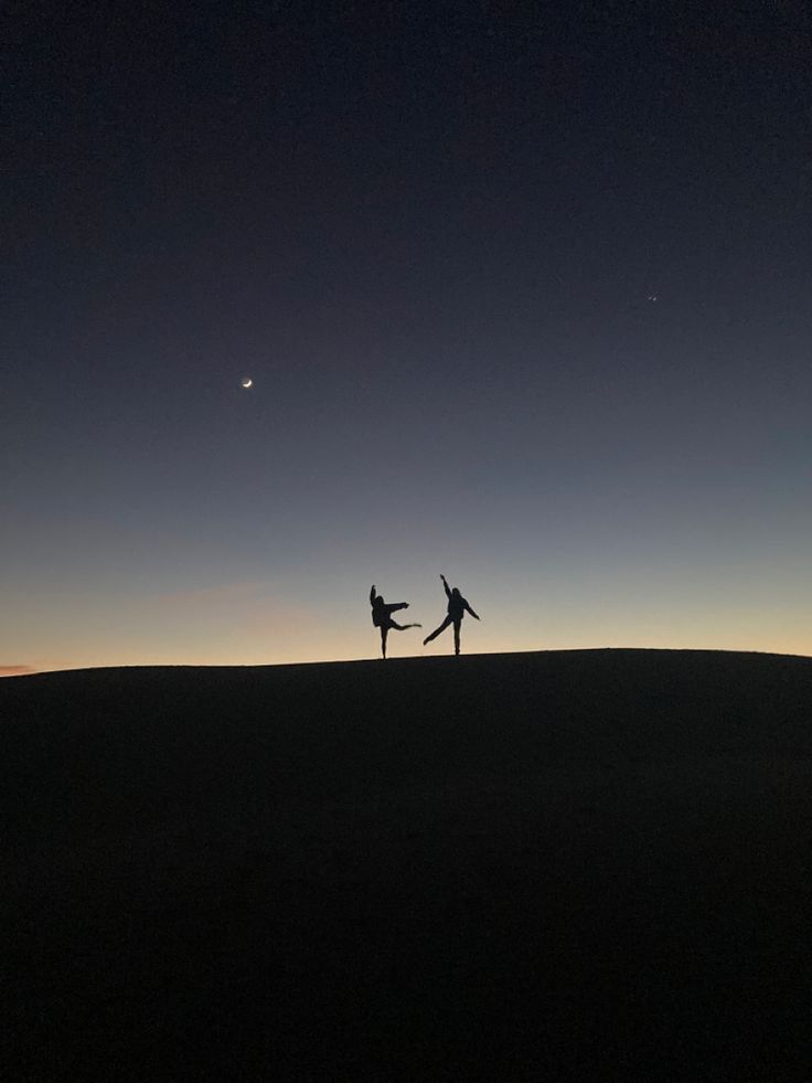 two people standing on top of a hill at night