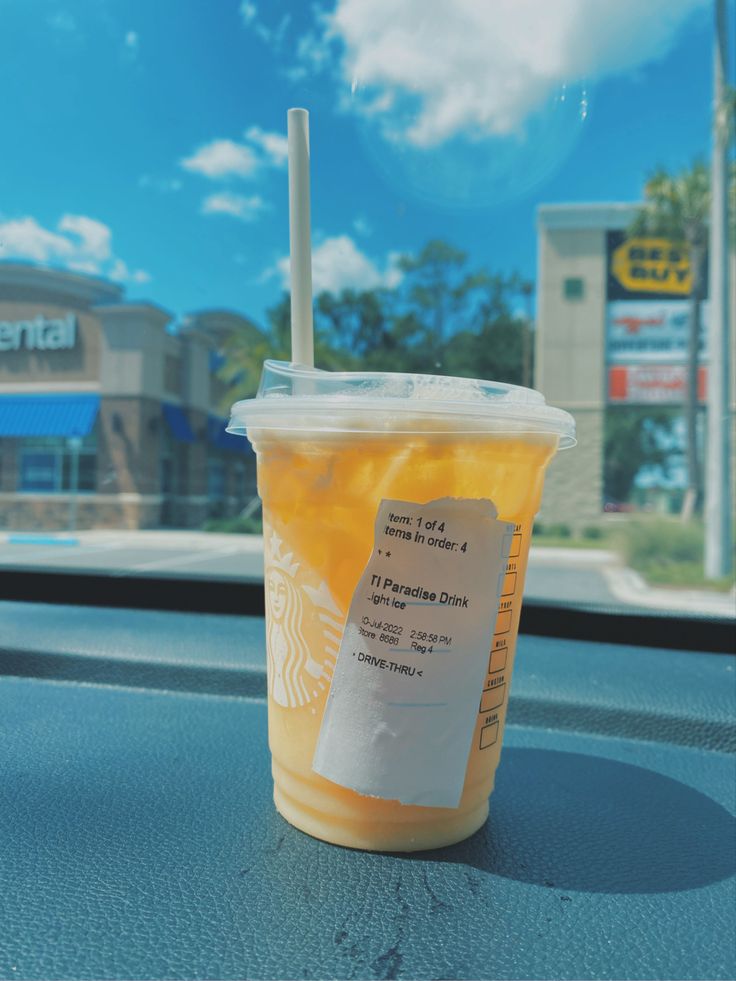 a plastic cup with a straw in it sitting on the dashboard of a car near a building