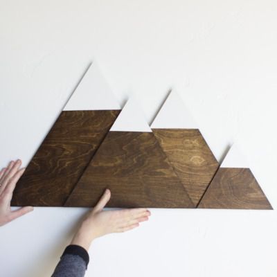 two hands are reaching up to the wall that has three wooden triangles on it