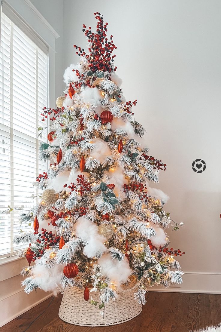 a white christmas tree decorated with red and gold ornaments in a basket on the floor