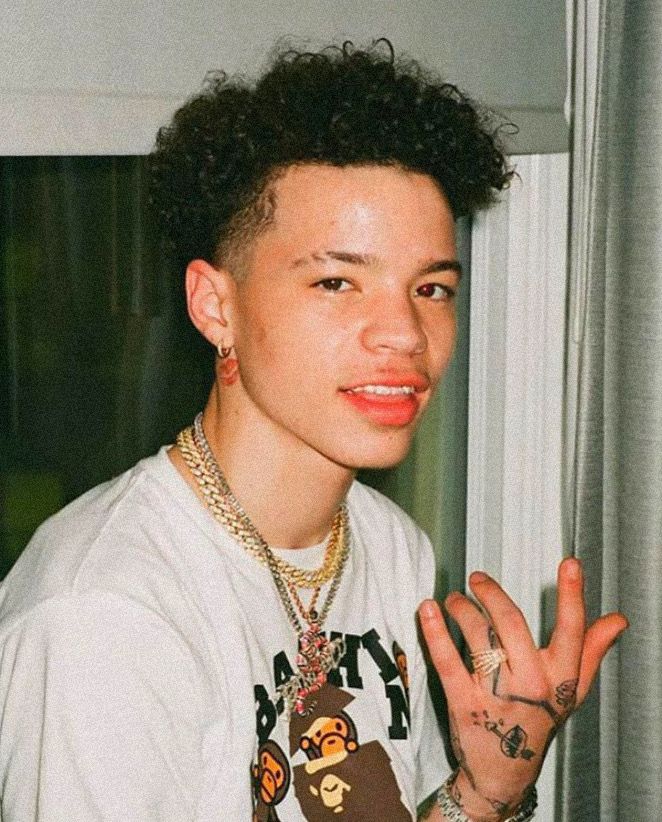 a young man with tattoos on his arm and hand in front of a window, wearing a white t - shirt