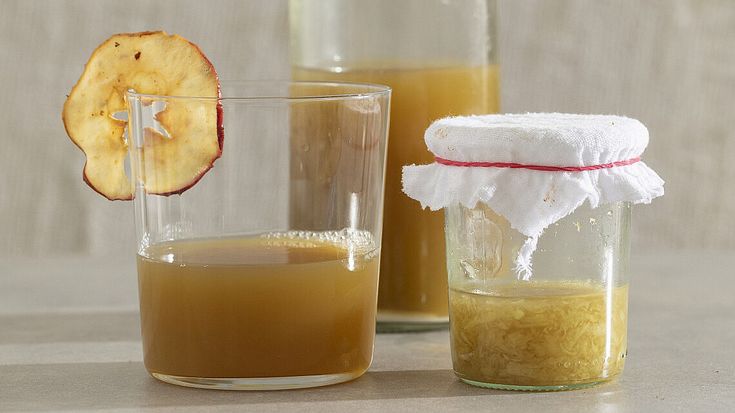 two glasses filled with liquid sitting on top of a table next to an apple slice